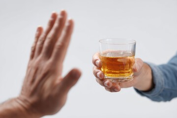 Hand gesturing stop towards a glass of amber liquid held by another hand on white background