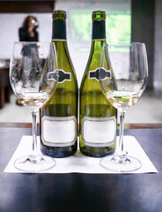 Two bottles of white wine with blank labels and glasses ready for tasting
