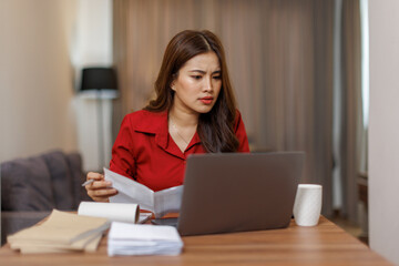 Happy asian woman using laptop while working remotely from home in living room
