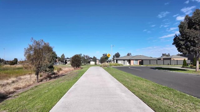 A footpath alongside a suburban road in Tarneit, Melbourne.A walkway bordered by native grasses and a residential housing estate. Concept of modern suburban infrastructure and planned community