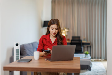 The work of a remote employee online. Young confident asian woman works with laptop analyzes startup project strategy at workplace home office.
