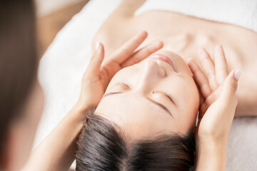 エステサロンで顔をマッサージされる若い女性