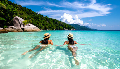 Two beautiful girls are playing in the crystal clear water on an island with a beautiful view on a clear, sunny day.