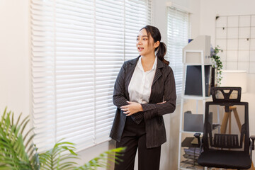 Smiling confident happy business asian woman with arms crossed standing in the home office.
