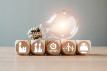 Light bulb with renewable energy icons on wooden blocks, symbolizing smart grid technology and...