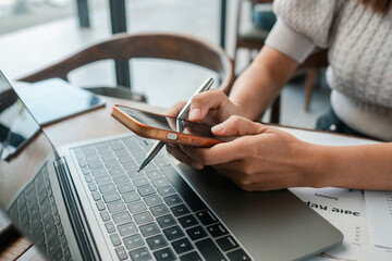 Professional woman multitasking with smartphone and laptop in a modern office environment, focusing on productivity.