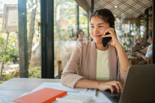 Professional woman multitasking with phone and laptop in a bright, modern office setting, showcasing productivity and communication.
