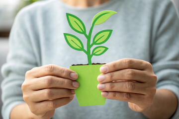 Person holding a green paper plant in a pot with both hands close to chest