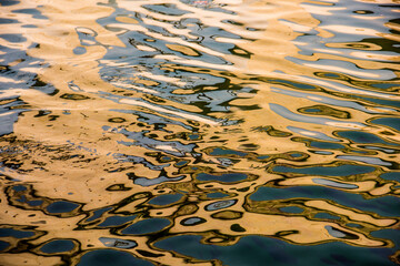 Water surface with moving wave of golden water reflecting sunlight