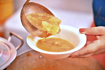 Cassava soup with pepperoni being served on a plate by a ladle