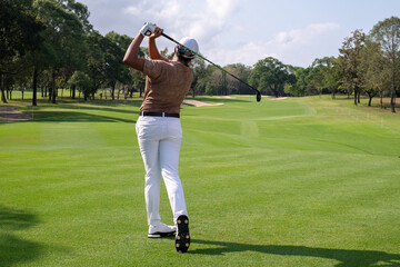 Professional female golfer lush green golf course, mid-swing after hitting a shot through after driving the ball down the fairway trees and distant sand bunkers, typical of a competitive setting.  