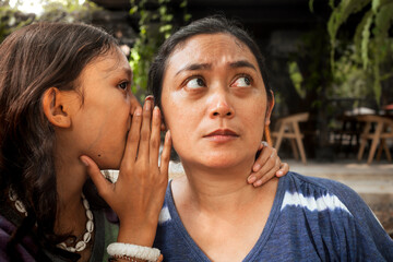 An Asian teenage girl whispering something to her mother's ear and her mother being a good listener. Intimate relationship between mom and daughter concept.