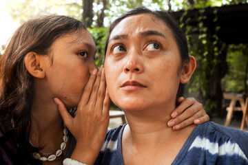 An Asian teenage girl whispering something to her mother's ear and her mother being a good listener. Intimate relationship between mom and daughter concept.