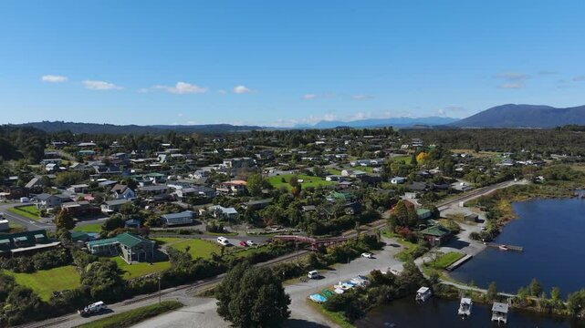 Aerial flyover port with parking boats at Lake Brunner and Moanta Town in New Zealand. Wide shot. Blue sky and sunny day on island. Railway track along coastline.