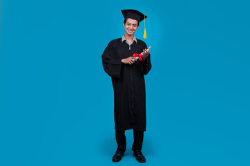 Full Length Portrait of Smiling Male Student in Graduation Gown Holding a Diploma Certificate