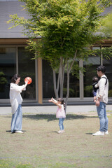 Fototapeta premium 平屋の戸建ての庭の前でボールを投げて遊ぶ家族と子供の幸せの不動産のファミリーイメージ 縦