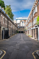 Narrow Alley Between Classic Brick Buildings Under Clear Sky, Featuring Historic Architecture and Small Residential Windows in a Peaceful Urban Setting.
