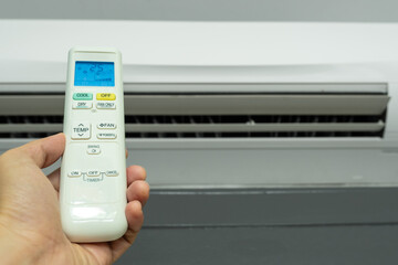 Man's hand using remote control open The air conditioner is cooled to 25 degrees Celsius in his...
