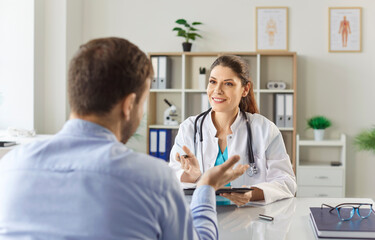 Obraz premium Young man patient talking to female doctor in her office in clinic during medical examination. Woman physician listening to the patient's complaints. Healthcare and medicine concept.