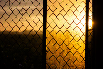 Chain link fence against a vibrant sunset sky, contrasting man-made barrier and natural beauty.

