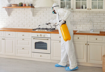 Professional worker in hazmat suit disinfecting kitchen indoor, insect killers, pandemic health...