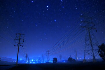 Power lines at night illuminated by blue lights in a starry sky, showcasing energy transmission and modern technology in rural landscape