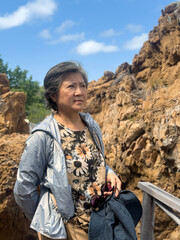 Naklejka premium Happy asian Thai elder woman standing in front of beautiful rock and beach view in Thailand.