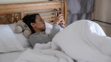 A young woman is lying on a hotel bed playing with her phone