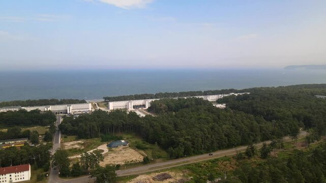 Aerial view over Prora on R&uuml;gen island, with its iconic seaside buildings stretching along the Baltic Sea coast, framed by dense forest.