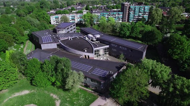High school building seen from above with rooftop full of solar panels surrounded by greenery in Dutch landscape and apartment complex behind