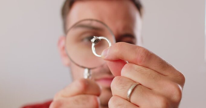 Jewerly inspect and verify. Jewelry appraiser looks intently at black gemstone ring held up to magnifying glass. Young man with serious, focused expression examines details of ring. Close up. 4K video