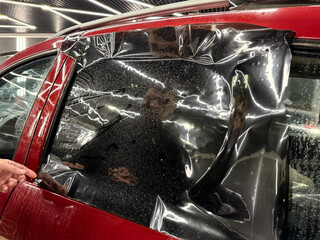 Applying tinting foil on a car window in the tuning studio close-up. Male car service worker glue...
