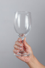 Hand holding empty wine glass by the base with fingers wrapped around clear transparent stemware...