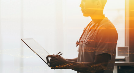 Healthcare professional using laptop with golden light effect overlay. Doctor with stethoscope reviewing digital medical data. Telemedicine and electronic health records. Modern healthcare technology