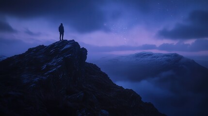 A solitary figure stands atop a rugged mountain peak, surrounded by mist and twilight sky. Nature&rsquo;s vast beauty unfolds in every direction.