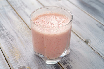 Fresh pink smoothie in clear glass on light gray wood background. Healthy refreshing drink for wellness and nutrition concept. Natural and organic beverage.