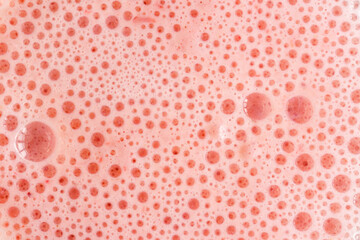 Pink foam texture with small bubbles on a light pink background. Close up macro view of liquid surface with air bubbles. Smooth beverage background abstract concept.