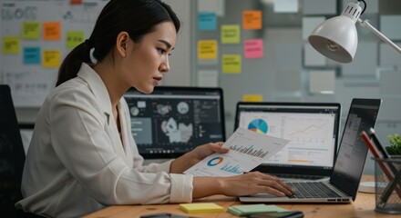 Focused young asian businesswoman analyzing data reports in modern office
