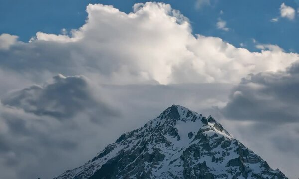 Snowy mountain with cumulus clouds in the cloudy sky