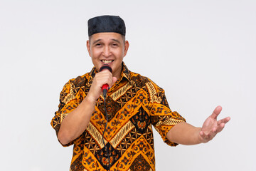 Smiling Indonesian man speaking into microphone while gesturing openly, wearing vibrant Batik shirt...