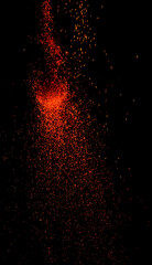 A vibrant firecracker bursts on the ground, scattering golden-orange sparks in all directions against a dark night backdrop. The glowing embers and smoke create a festive, celebratory atmosphere.