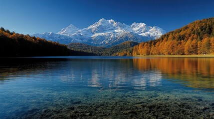 Fototapeta premium Serene alpine lake reflecting snow-capped peaks. Autumn foliage lines the shore
