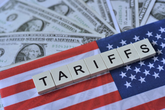 " Tariffs" wooden word on US flag with US dolla bills background. US new import taxes announced by Donal Trump. Affected to baseline tariff, reciprocal tariffs, deminimis rule impack on global economy