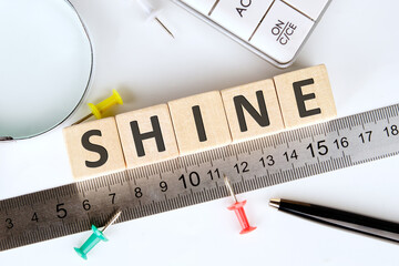 SHINE word written on wooden cubes, arranged according to a ruler using a magnifying glass and...