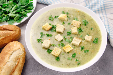 Homemade cream soup with chicken and herbs in a white plate on a gray background.