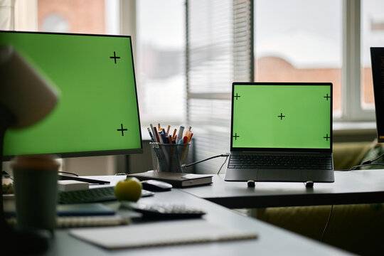 Multiple screens with tracking markers visible in modern office setting featuring gadgets and electronics surrounding workspace. Window in background letting natural light into room