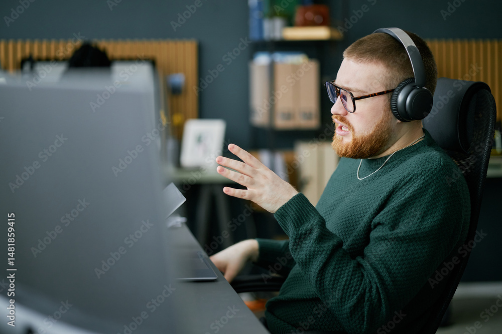 Poster man wearing glasses and headphones, working on computer at desk in modern office. bookshelf and wall