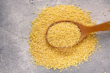 Millet grains in wooden spoon on a gray background