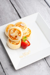 Delicious sweet cottage cheese pancakes served with fresh strawberries and cream on a white plate for breakfast