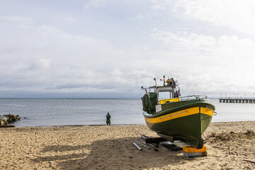 Obraz premium A man fishes quietly at the edge of the sea, his boat resting patiently beside him